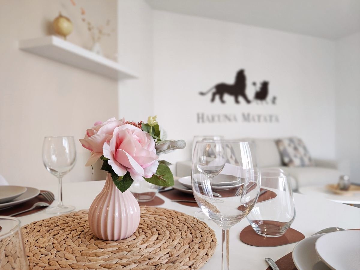 Table dressée et canapé clair du séjour de CasaSimba, sous le sticker mural « Hakuna Matata »